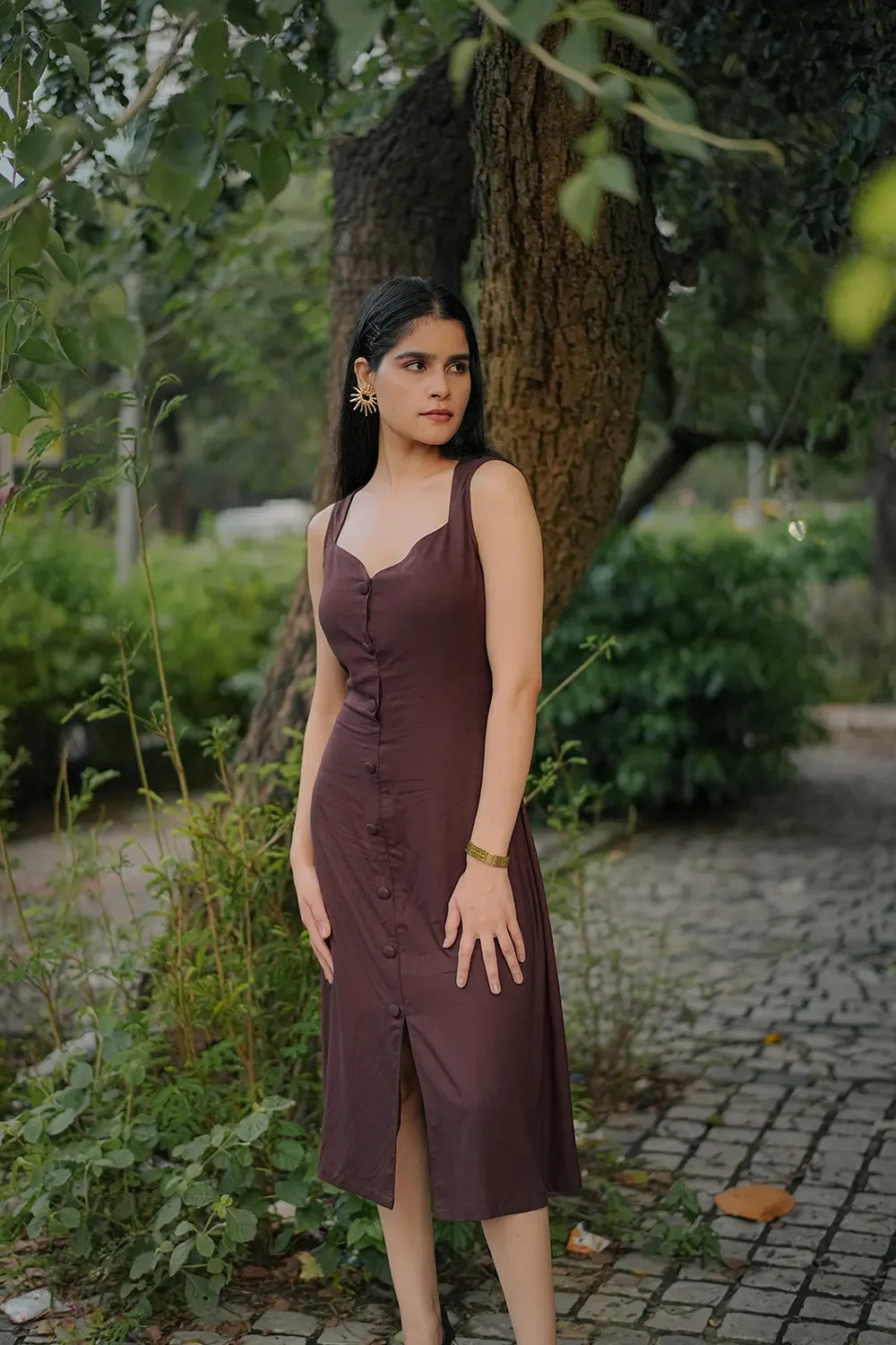 Woman in a sleeveless brown button-front dress standing outdoors by a tree, Streiq fashion