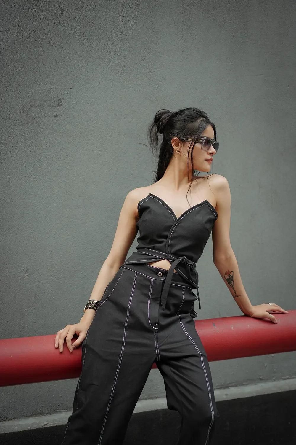 Woman in black sleeveless jumpsuit posing outdoors against gray wall, Streiq fashion