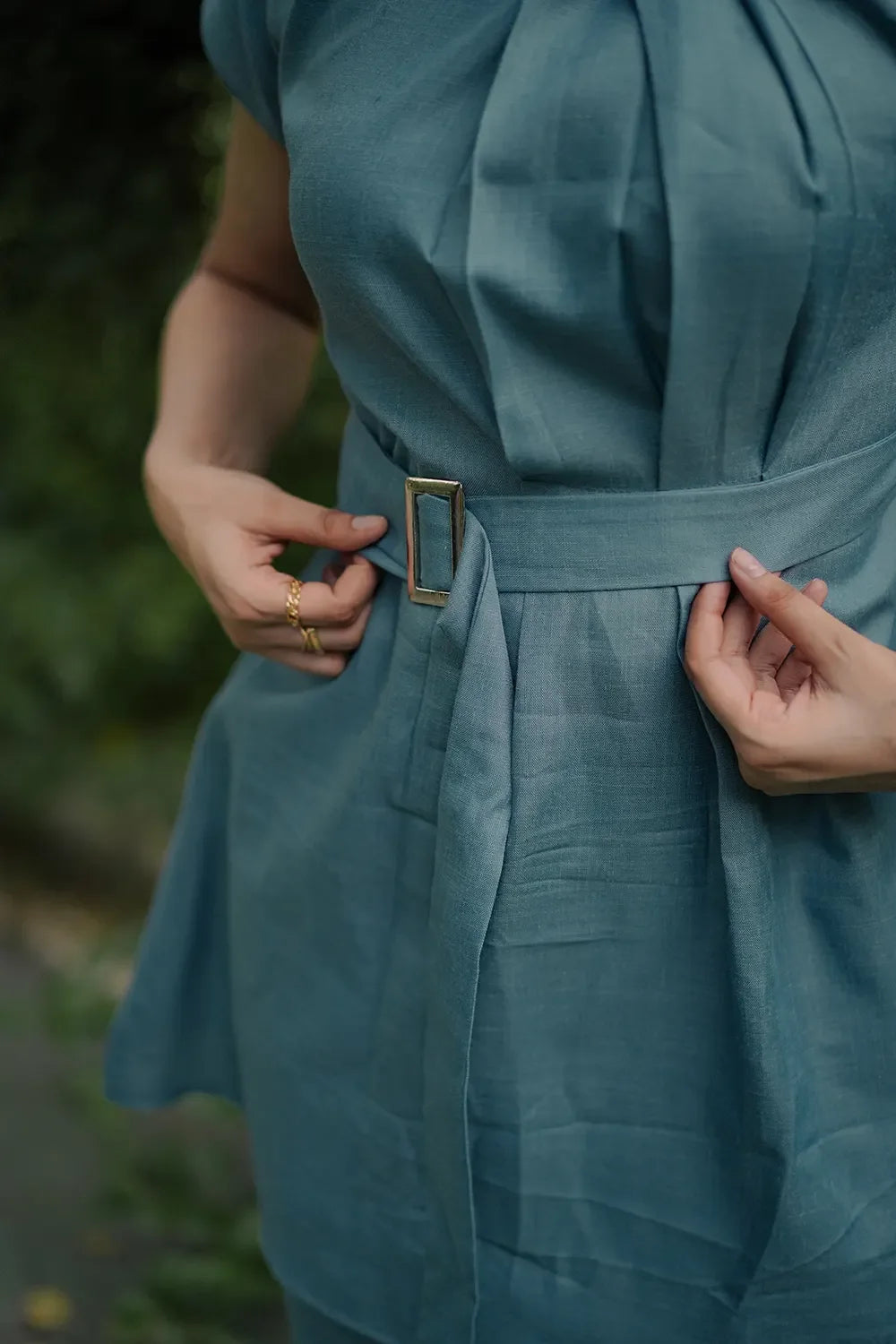 Close-up of a person adjusting a belted teal dress, Streiq fashion detail