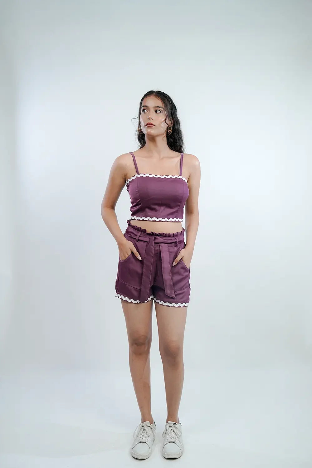 Woman modeling purple crop top and shorts set with white trim from Streiq on plain background