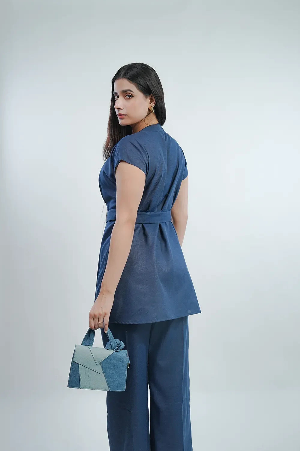 Woman in blue belted tunic and wide-leg pants holding a denim handbag, Streiq fashion