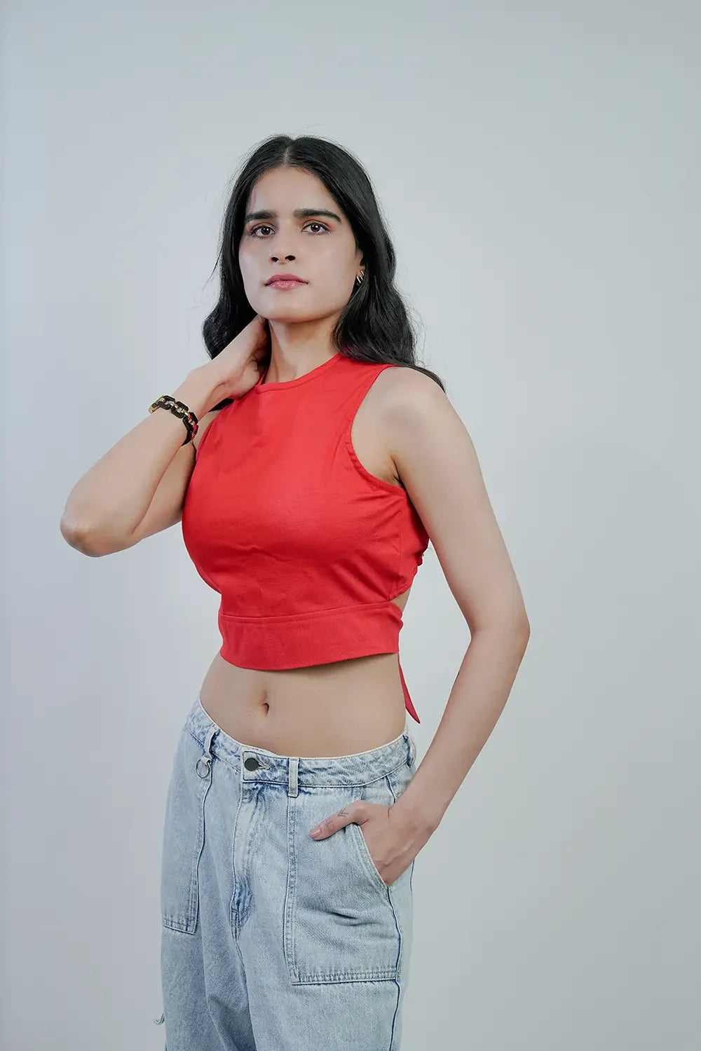 Woman wearing red sleeveless crop top and light blue jeans against plain background