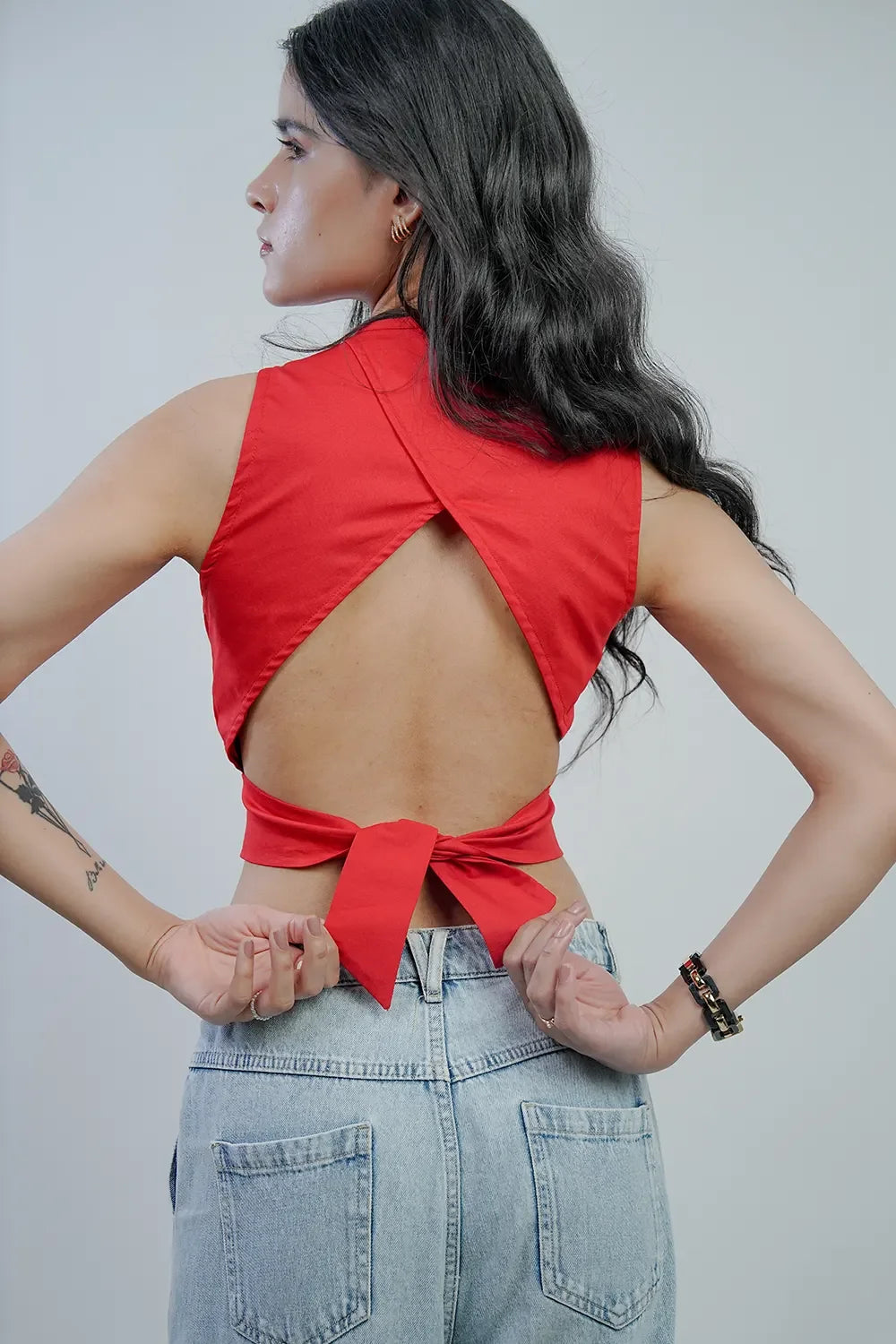 Woman in Streiq red open-back top with tie detail and light blue jeans, back view