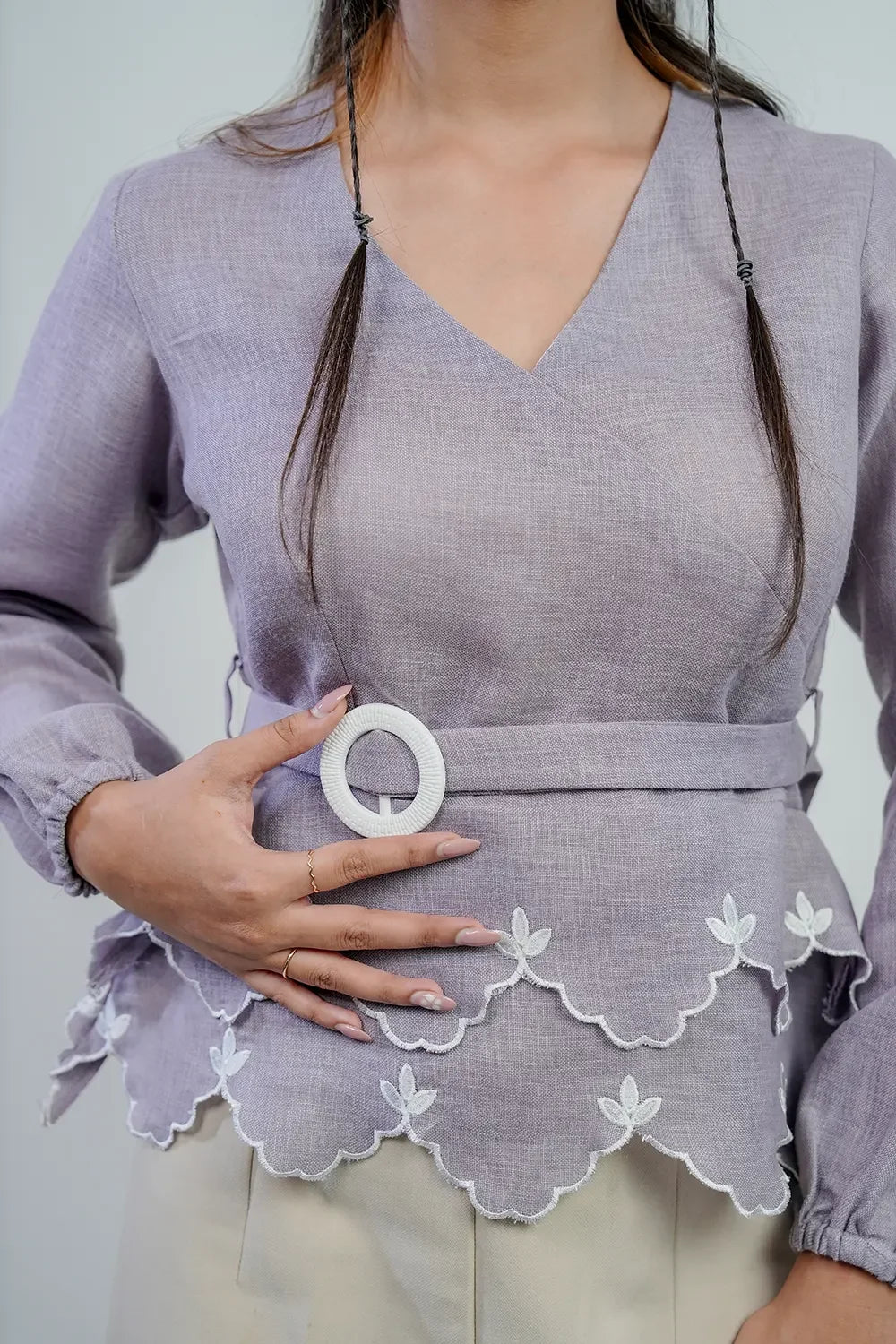 Woman wearing a lilac blouse with scalloped hem, floral embroidery, and belt detail from Streiq