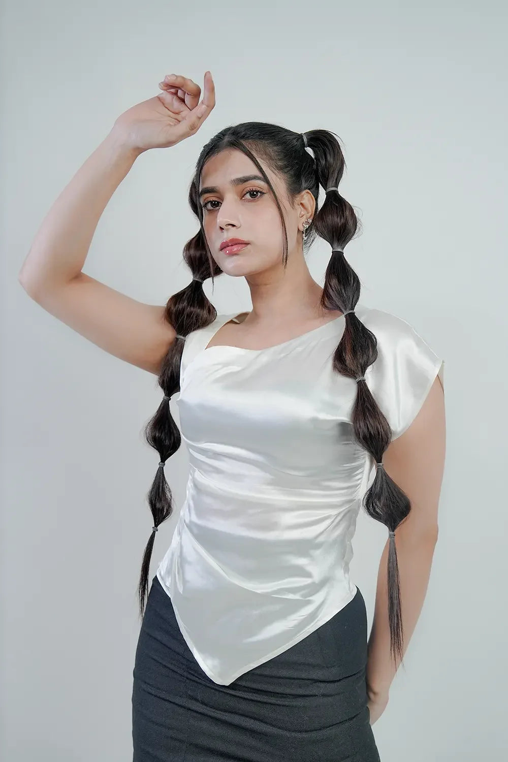 Woman in unique white satin asymmetrical top with bubble pigtails, minimal background