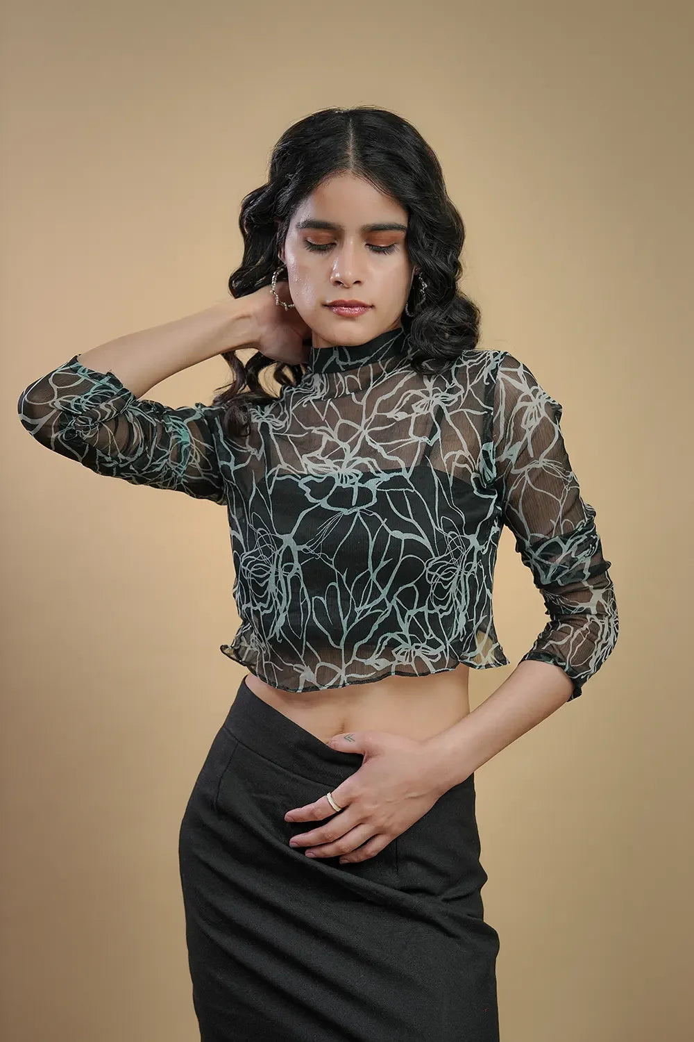 Woman in sheer floral mesh crop top and black skirt from Streiq against a beige background