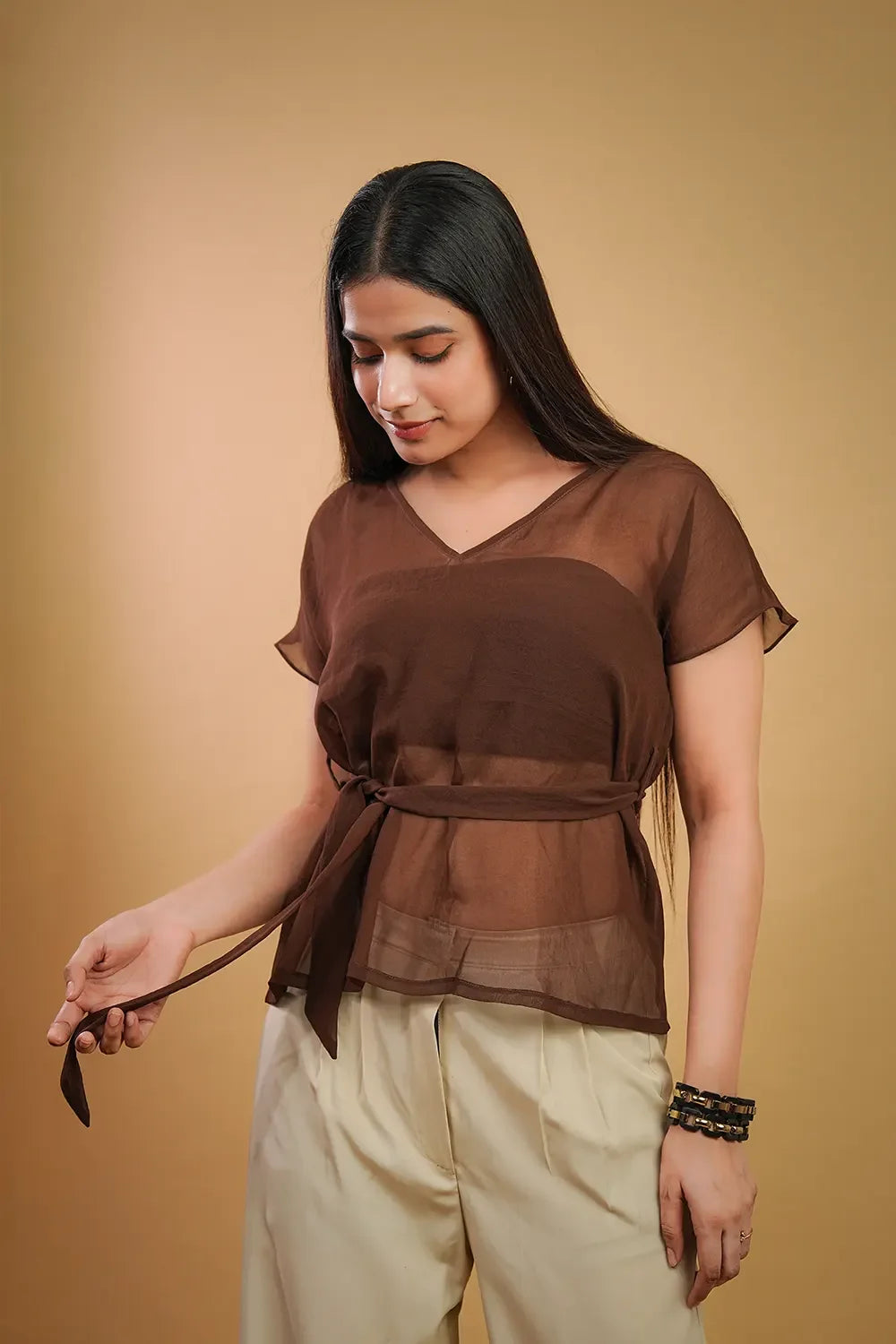 Woman wearing a sheer brown V-neck top with belt and cream trousers, Streiq fashion