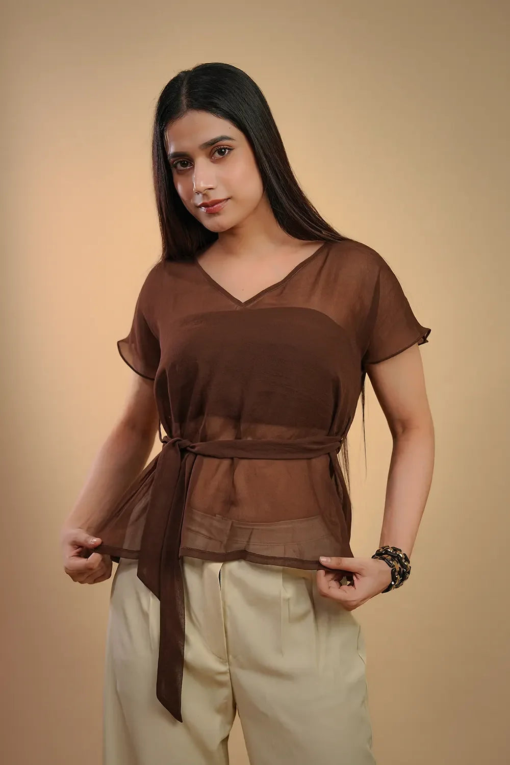 Woman wearing a brown sheer belted top and cream pants, Streiq fashion style