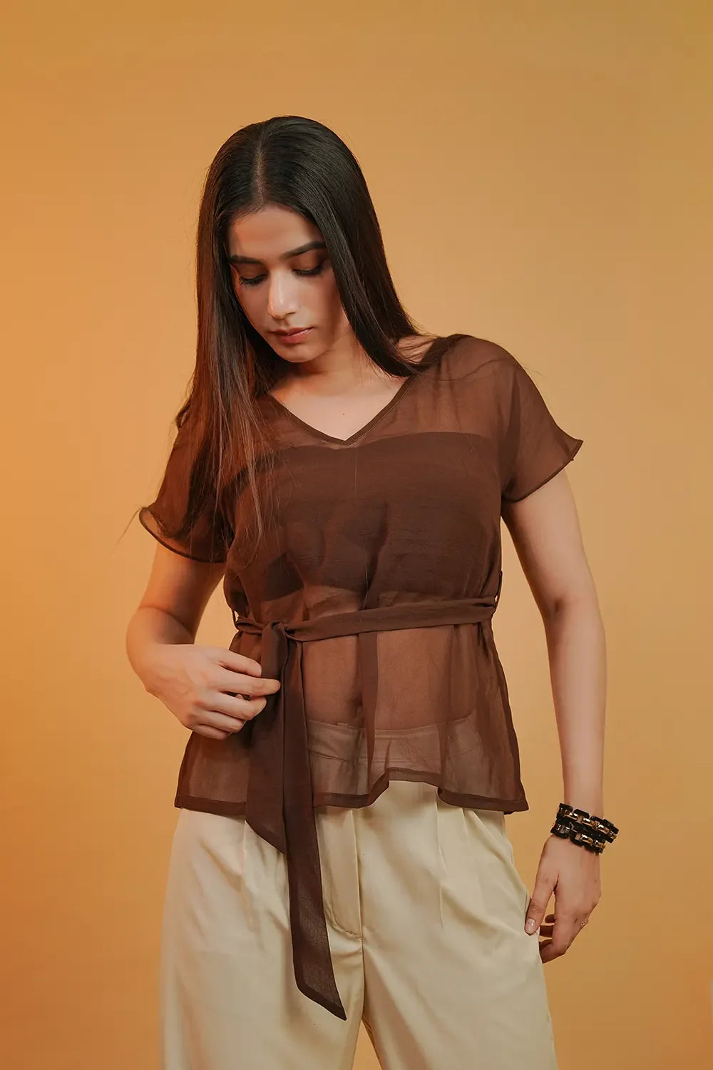 Woman wearing sheer brown belted top and cream pants, Streiq fashion, neutral background