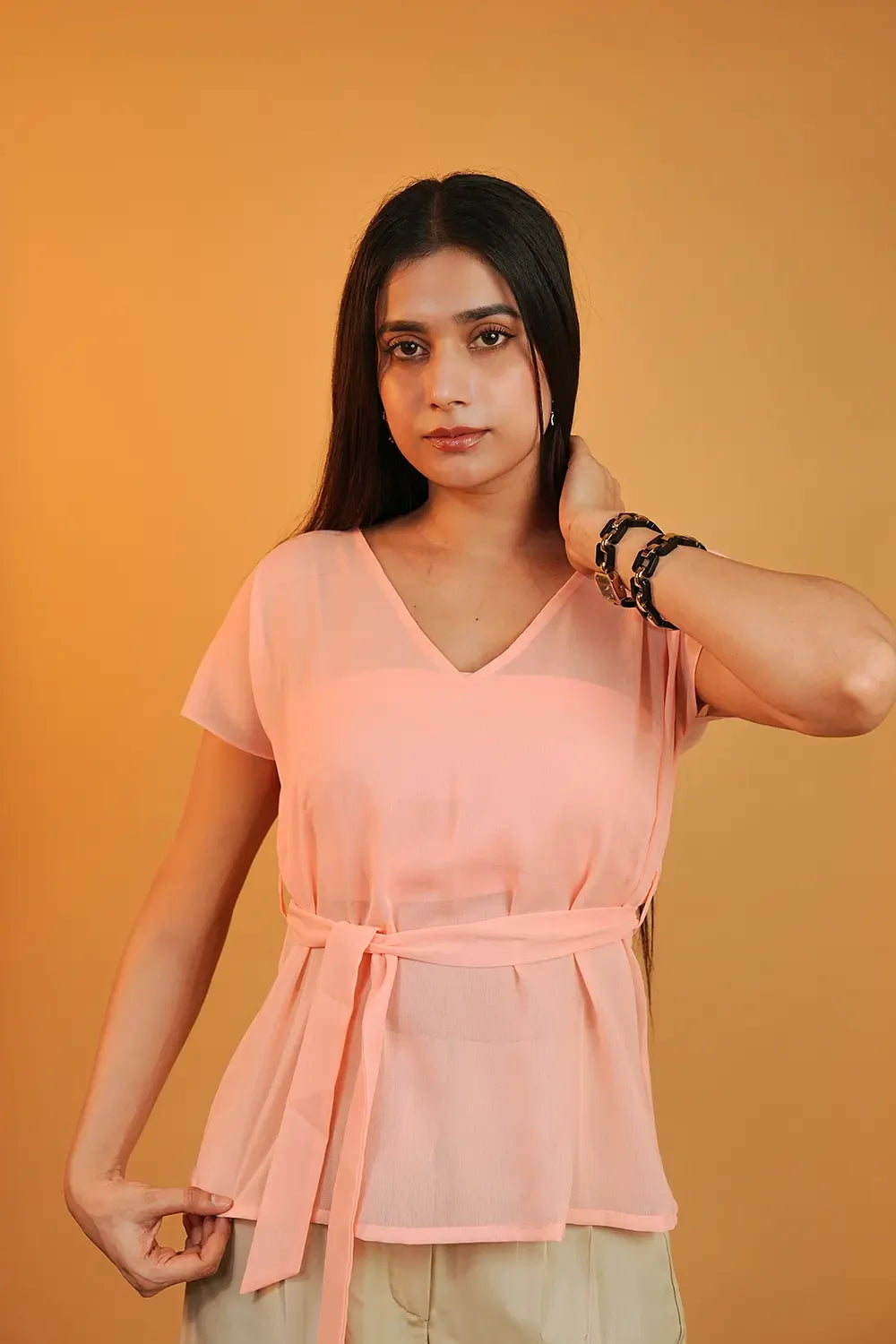 Woman in a peach belted blouse from Streiq, standing against a solid orange background