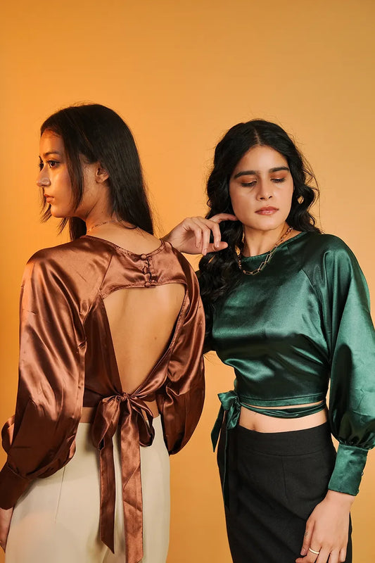 Women modeling Streiq satin blouses in emerald green and copper brown with tie-back details