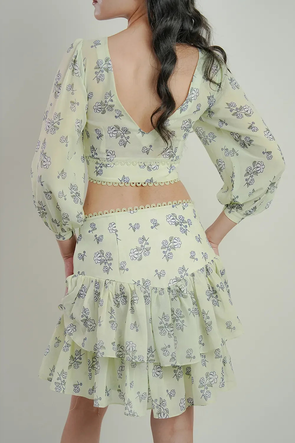 Back view of woman wearing light green floral print dress with ruffled skirt, Streiq fashion