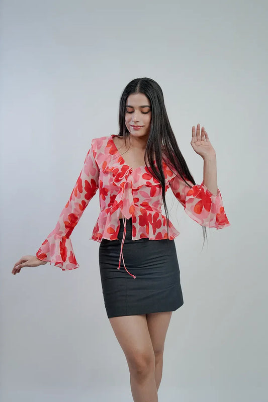 Woman in a red floral ruffle blouse and black mini skirt posing against a plain background