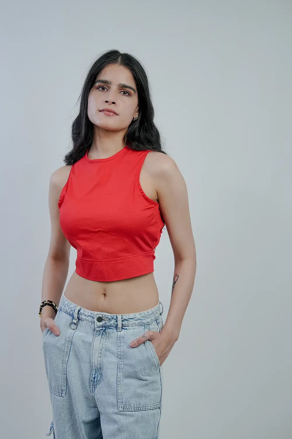 Woman in a red sleeveless crop top and light denim jeans against a plain background