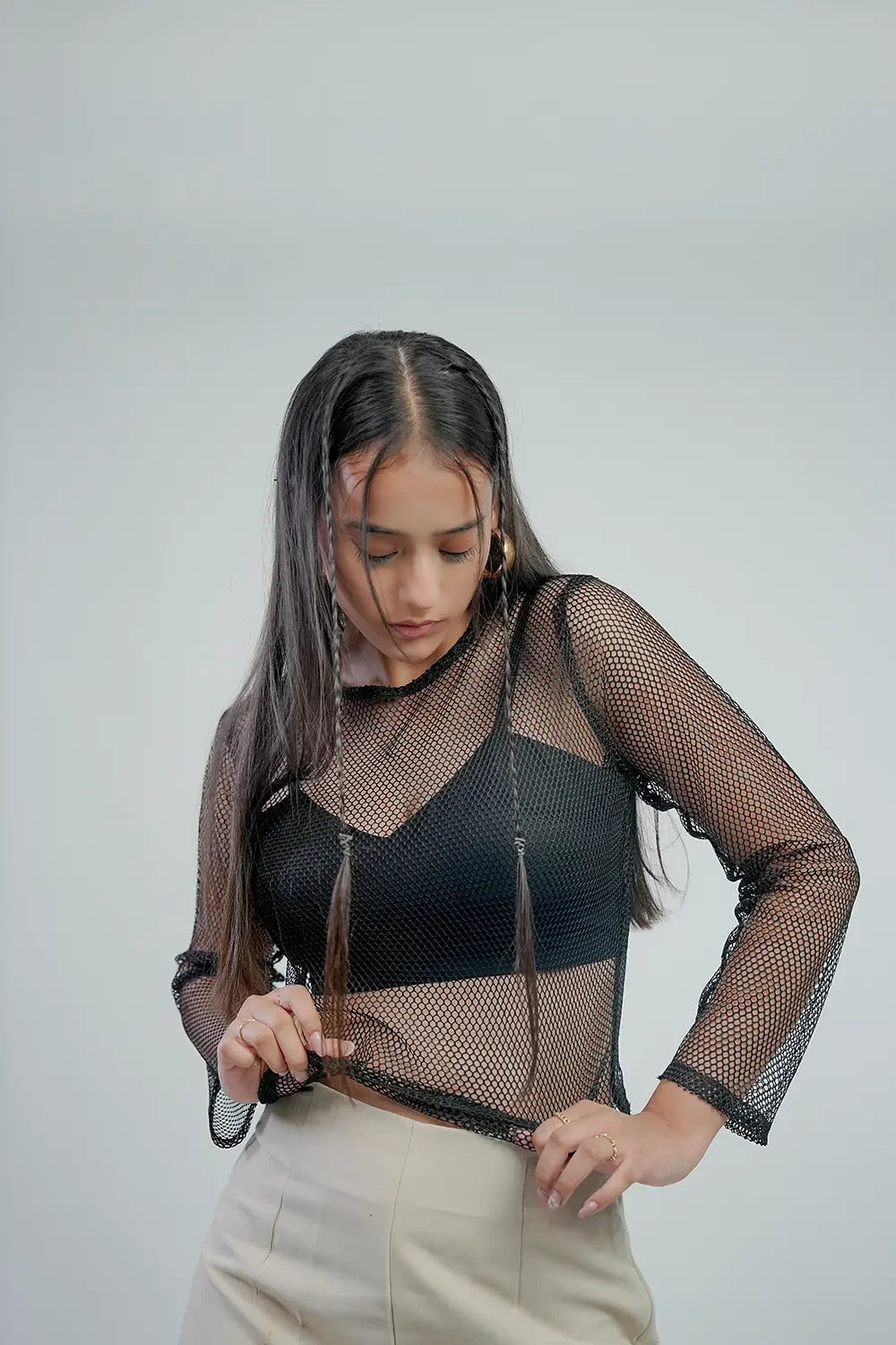 Woman in black mesh top and beige trousers, Streiq fashion, minimalist studio background