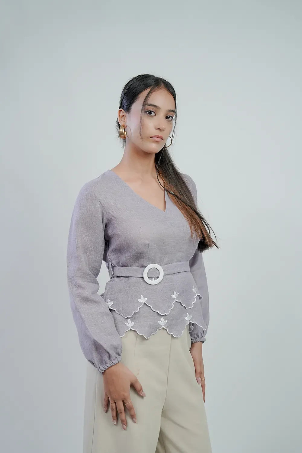 Woman in lilac long-sleeve belted top with scalloped hem, cream pants, at Streiq