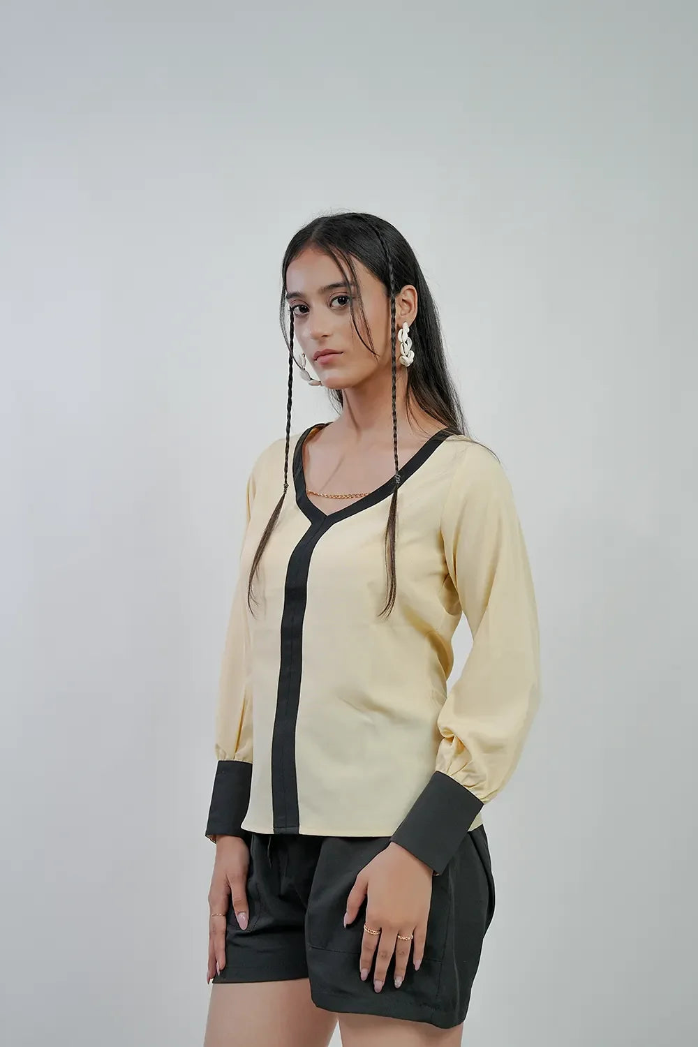 Woman in a beige blouse with black accents and black shorts, posing for Streiq fashion