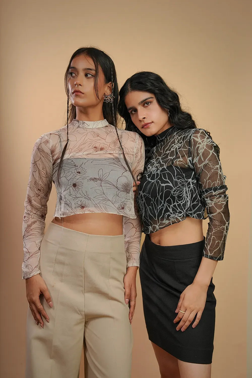 Two women in Streiq sheer floral long sleeve crop tops, posing against a beige backdrop