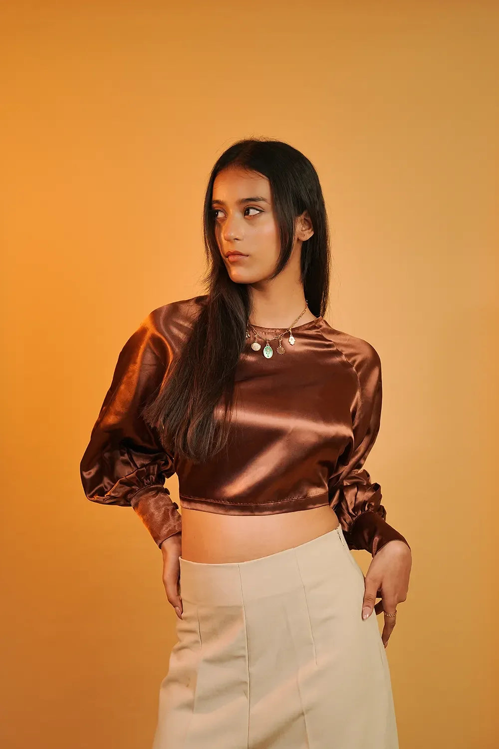 Woman in brown satin crop top and beige skirt, Streiq fashion, orange background