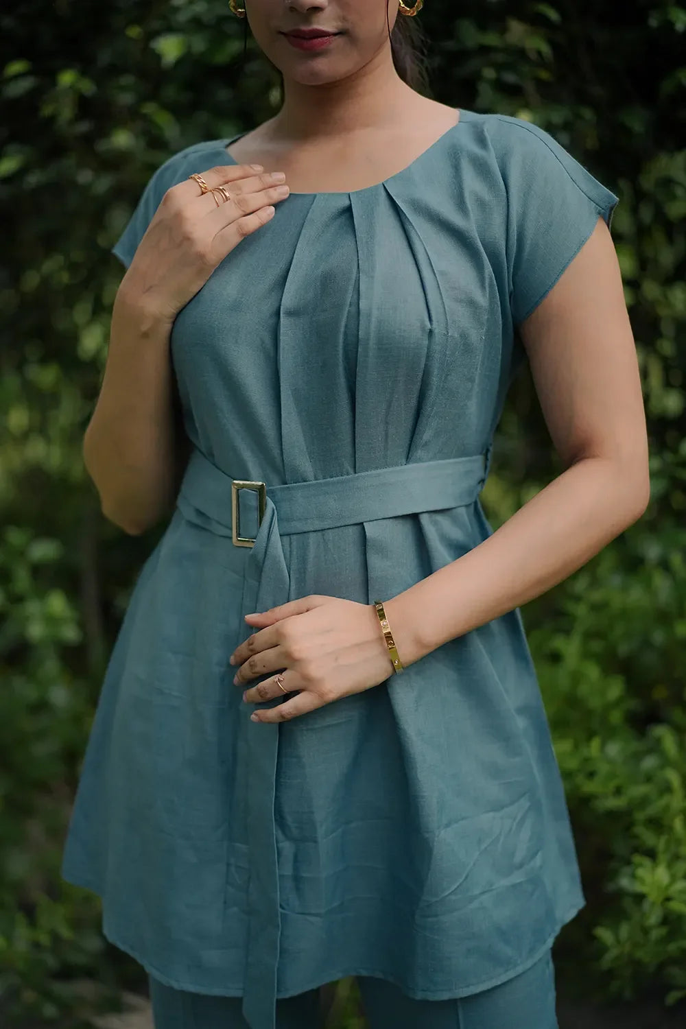 Woman wearing teal belted tunic top with pleats, gold jewelry, outdoors, Streiq fashion